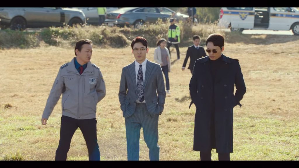 Three men walk towards the camera - the ones who look like cops are wearing a suit and a trench coat along with a pair of glasses and a pair of aviators