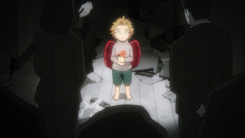 Hawks in the past as a little boy, surrounded by people in suits, holding a tiny Endeavor doll in his hands