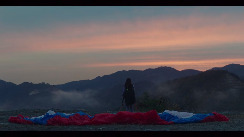 Se-ri looking over a cliff with her parachute spread out behind her